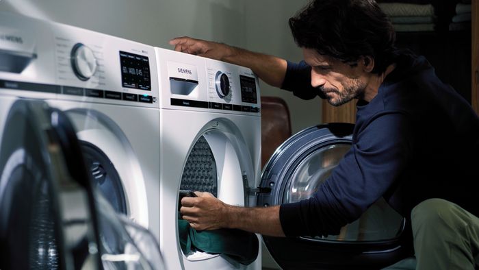 Ein Mann entnimmt Wäsche aus einem Siemens Wärmepumpentrockner mit großem Fassungsvermögen.