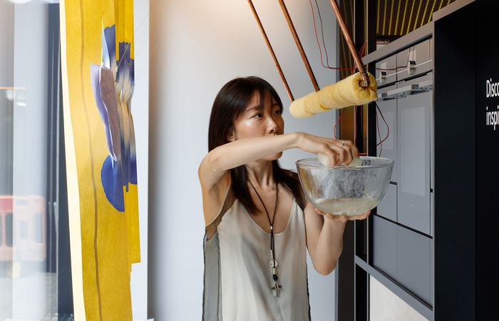 Woman mixing ingredients in a bowl, with suspended kitchen equipment in a unique setting.