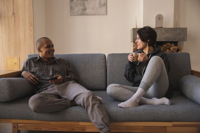 Mężczyzna i kobieta siedzący na szarej kanapie, kobieta trzyma w ręce szklankę z białą kawą.