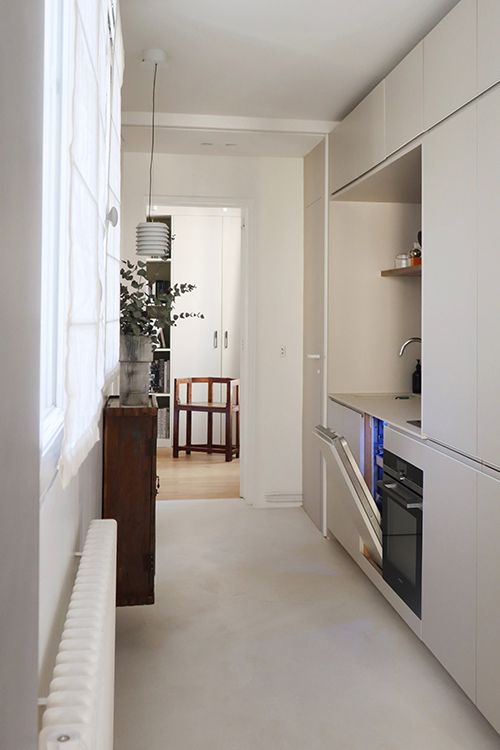 Intérieur de cuisine minimaliste avec armoires blanches, appareils électroménagers et une fenêtre offrant une lumière naturelle.