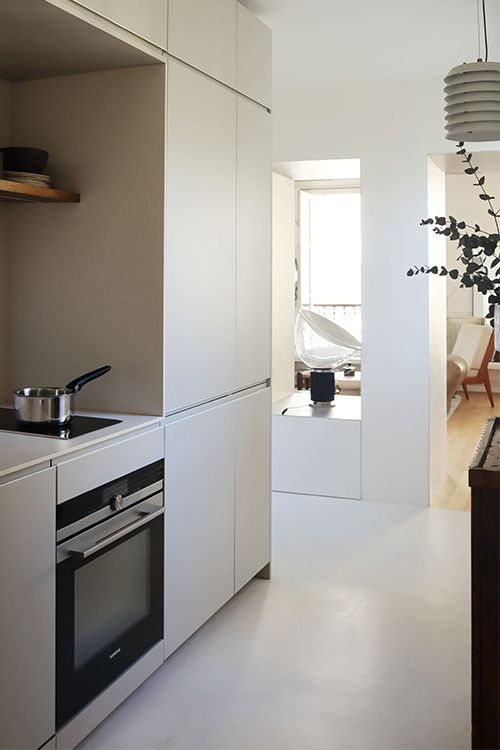 Cuisine moderne avec armoires blanches, étagères et appareils électroménagers dans un intérieur lumineux et minimaliste.