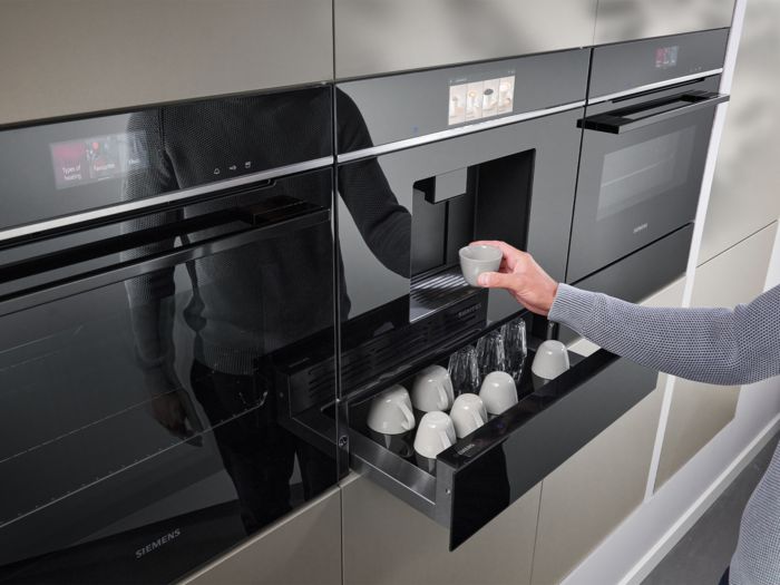 Una cucina moderna con eleganti elettrodomestici Siemens, tra cui un forno e una macchina per il caffè, con una persona che versa il caffè in una tazza.