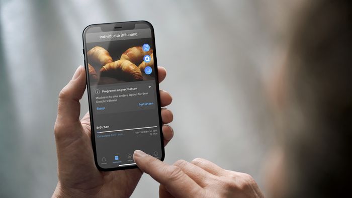 Eine Person hat ein Smartphone in der Hand auf der eine Einstellung der Home Connect App zu sehen ist 