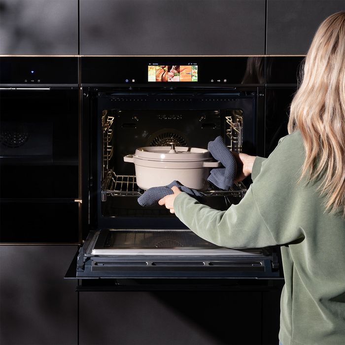 Donna che estrae una pirofila con coperchio dal forno Siemens