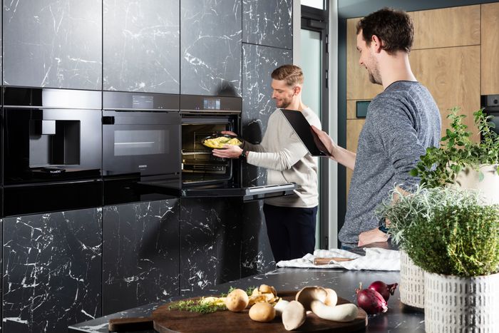 Coppia di ragazzi in cucina che interagisce con il forno della linea studioLine di Siemens