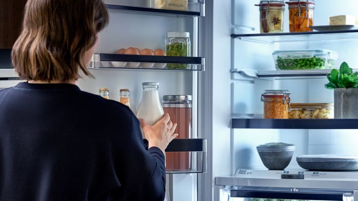 Donna che prende una bottiglia di latte da un frigorifero aperto ben rifornito