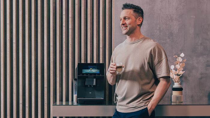 Alexander Kumptner, der Koch Influencer, genießt einen Kaffee neben einem Siemens Kaffeevollautomaten.