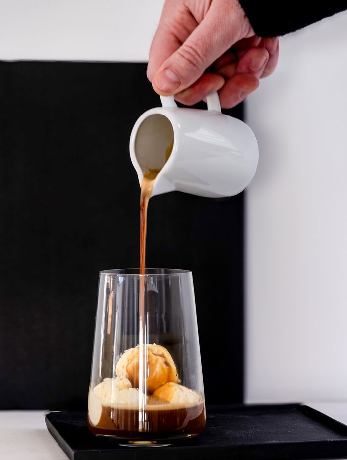 Drie bolletjes vanille-ijs in een glas. Een hand houdt een blikje espresso vast en giet het over het ijs. Een eenvoudig maar lekker koffierecept.