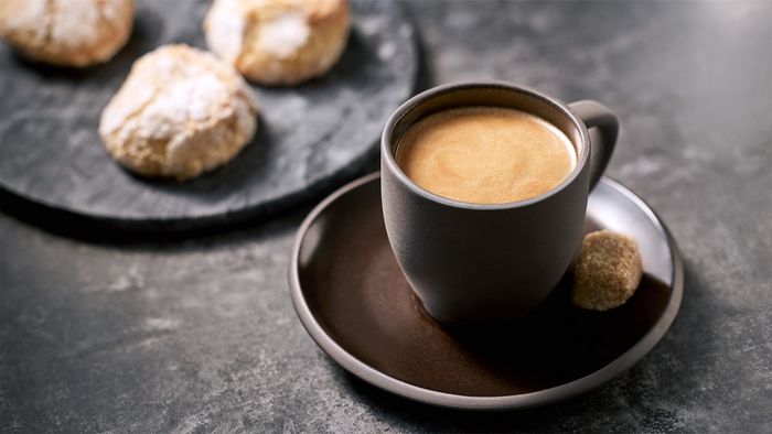 Italienischer Moka in einer dunklen Tasse mit einem Stück Würfelzucker.