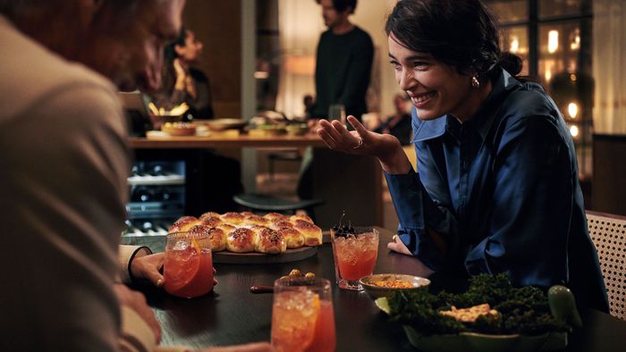 Un'accogliente riunione con persone che gustano cocktail e una serie di piatti, tra cui involtini e una vivace insalata sul tavolo.
