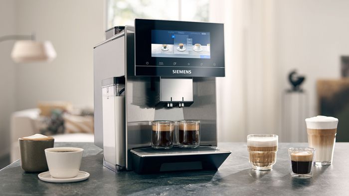 Ein Siemens EQ900 Kaffeevollautomat, daneben unterschiedliche Kaffeespezialitäten.