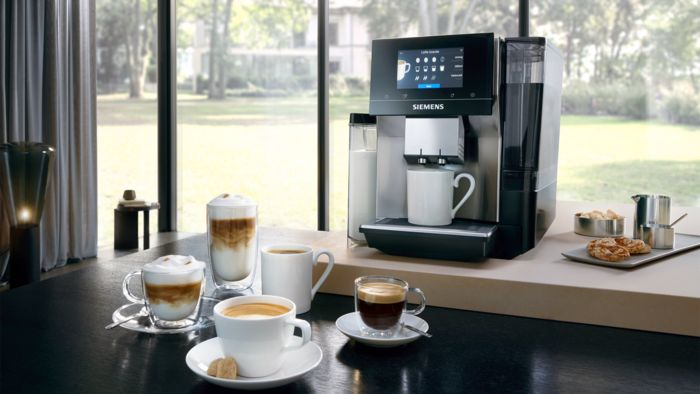 Ein Siemens EQ700 Kaffeevollautomat, daneben unterschiedliche Kaffeespezialitäten.