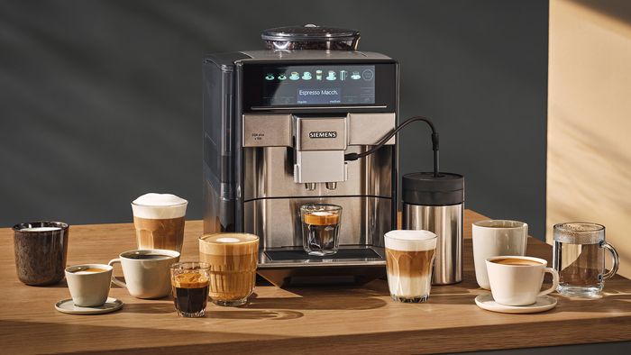 Ein Siemens EQ6 plus Kaffeevollautomat, daneben stehen verschiedene Kaffeespezialitäten.