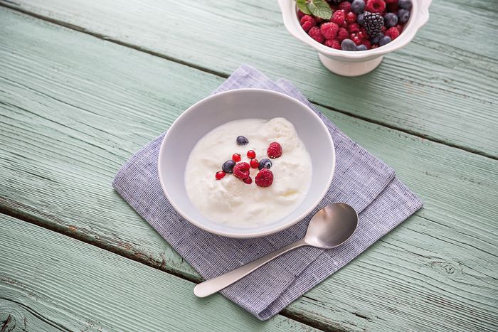 Una ciotola di yogurt cremoso con lamponi freschi, mirtilli e ribes rosso, accanto a un cucchiaio d'argento su un tovagliolo blu.