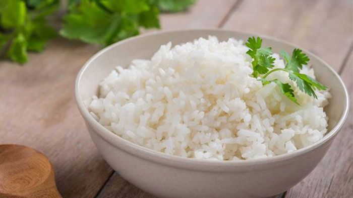 Tazón de arroz blanco cocido adornado con perejil fresco en la mesa de madera.