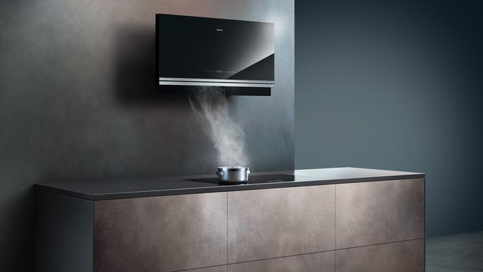 Moderne keuken met zwarte wand afzuigkap en stoom die uit een pot op de toonbank komt.