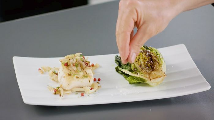 Piatto con trancio di pesce e mano che aggiunge il sale sulle verdure