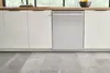 Modern kitchen with Bosch stainless steel dishwasher, white cabinets, and gray tile flooring.