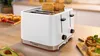 Weißer Bosch-Toaster auf Holzoberfläche, mit Chrom-Akzenten und Schlitzen für Brot.