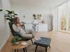 Personne se relaxant dans un fauteuil, les pieds sur un pouf, tenant une tasse dans une cuisine ouverte et confortable.