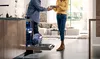 A man and woman stand together in a kitchen, next to an open dishwasher filled with clean dishes.