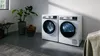 A laundry room featuring a white washing machine and dryer, with a potted plant and soft textiles in a bright, minimalist space.