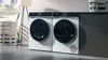 A laundry room featuring a white washing machine and dryer, with a potted plant and soft textiles in a bright, minimalist space.