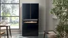 A modern kitchen featuring a sleek black fridge, stylish wine cooler, and organized shelves with decorative items.
