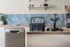 Modern kitchen countertop with a dishwasher, cutlery holder, wine glass rack, blue tiled backsplash, and minimal decor.