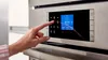 Person using a Bosch wall oven touch control panel with a digital display showing settings.