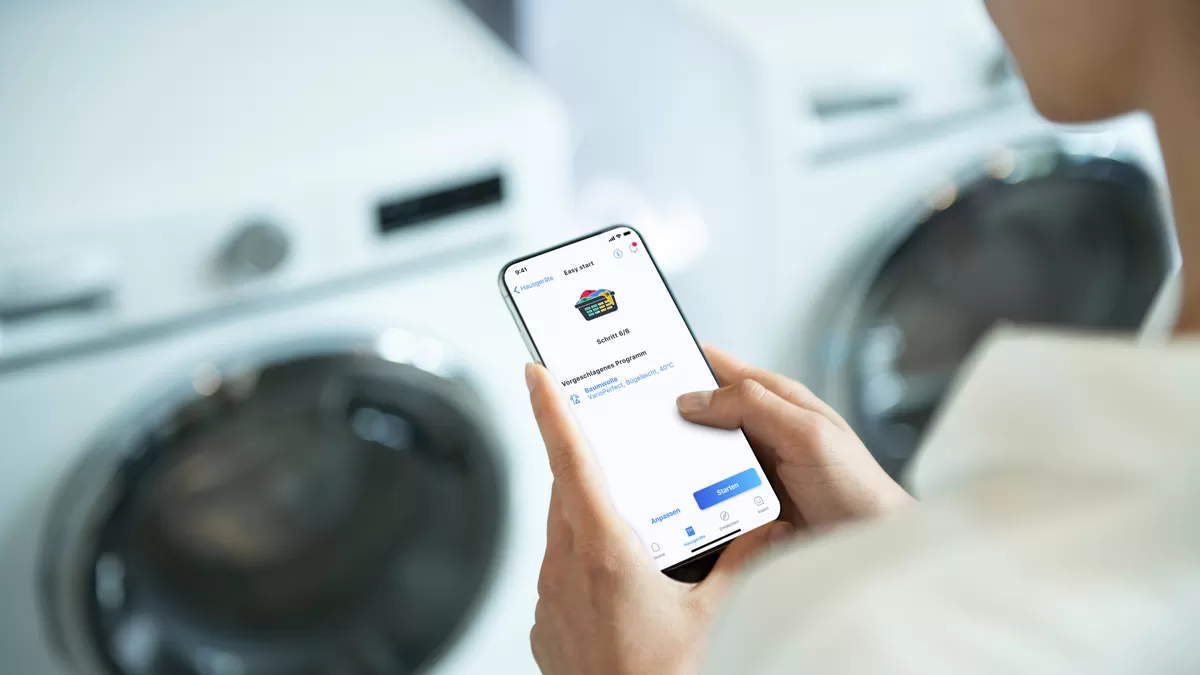 Çamaşır makinesine yakın akıllı telefon uygulamasını kullanan kişi.