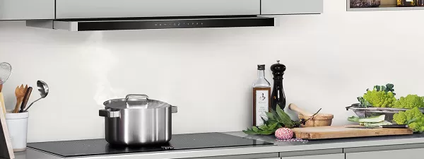 Moderne Küchenarbeitsplatte mit Dampftopf, Kochutensilien, mit automatischem Luftsensor für die flache Dunstabzugshaube und darüber liegendem Schrank.