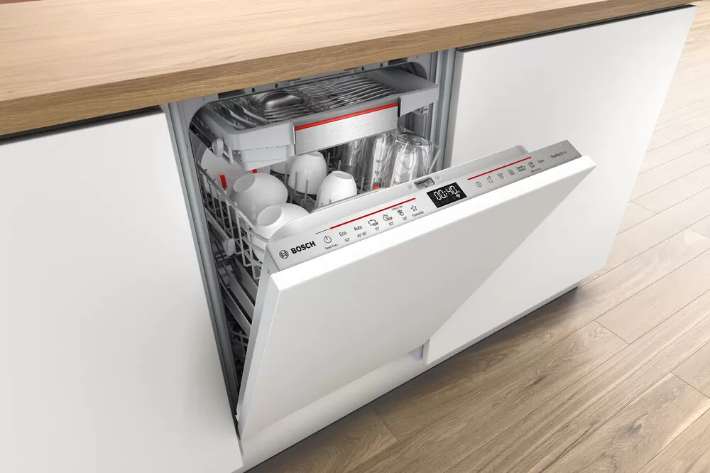 Un lavavajillas Bosch con la puerta abierta, mostrando platos, tazas y vasos ordenados en su interior, situado en una cocina moderna.
