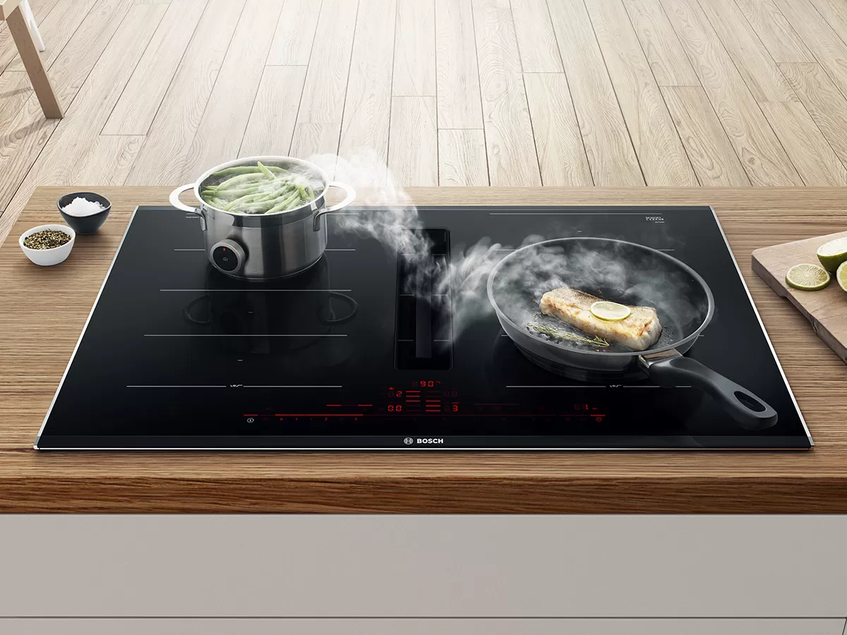 Induction cooktop with steaming pot andscalezling pan, mutfak malzemeleri ile ahşap yüzeyde çevrili.