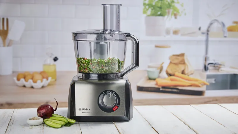 Bosch processor blends veggies on counter, eggs and carrots behind in sleek modern kitchen.