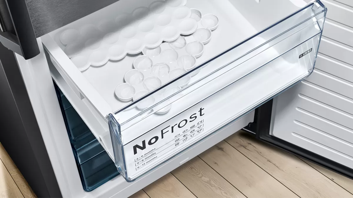 A refrigerator drawer labeled "NoFrost" contains ice cube trays, set on a wood floor, showcasing a modern kitchen design.