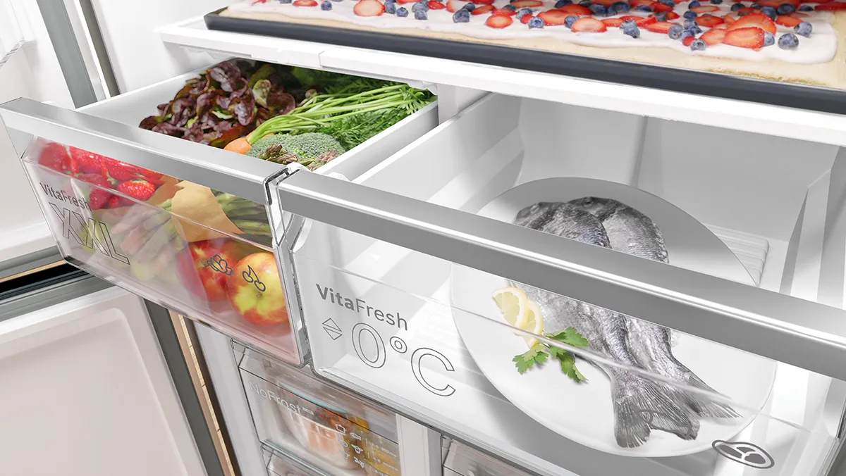 Eine Nahaufnahme eines modernen KUhlschranks, der frisches Obst, GemUse und Fisch zeigt, die in transparenten Schubladen bei optimaler Temperatur gelagert werden.
