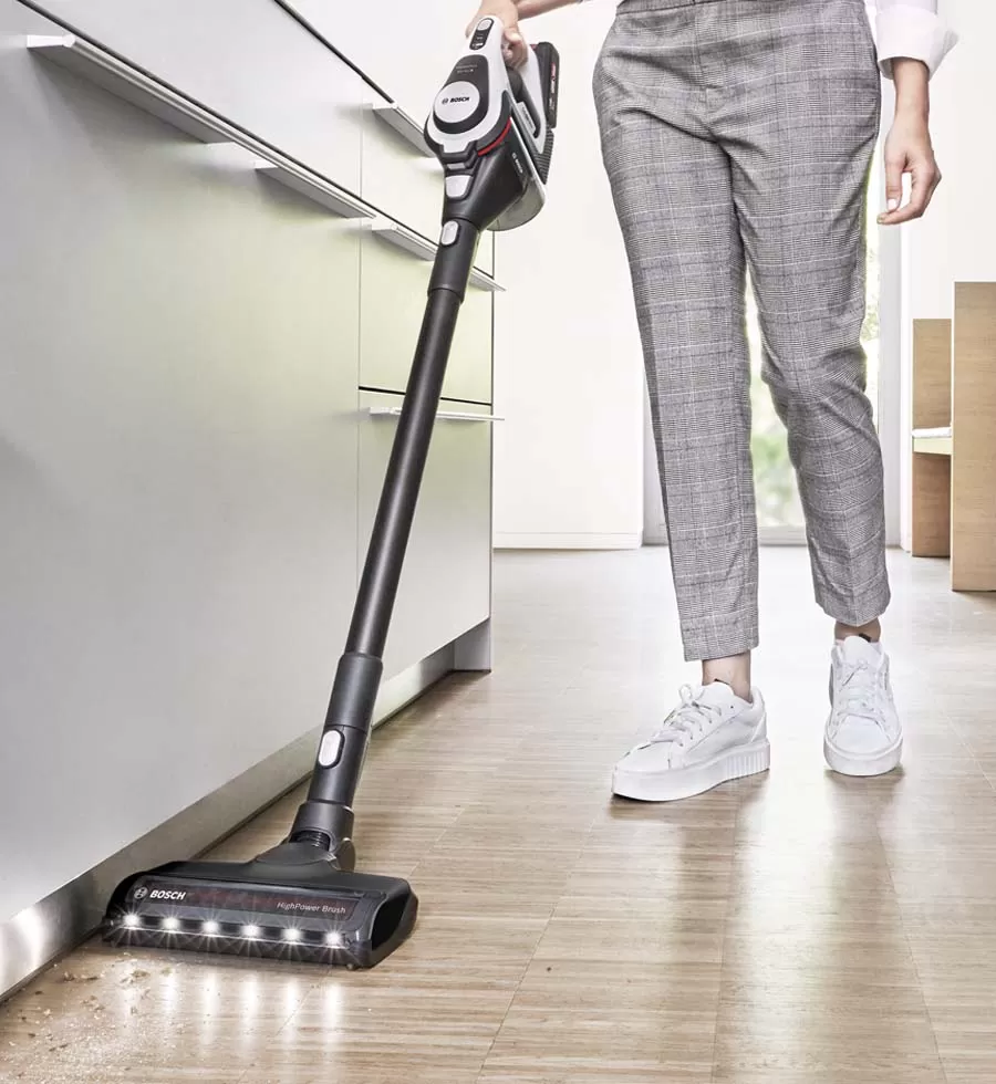 A woman uses a cordless vacuum to clean up a mess on a cream rug in light, bright living room.