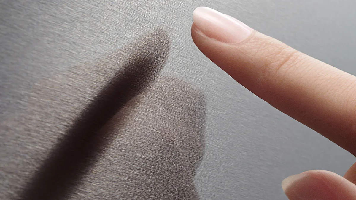 Eine Nahaufnahme eines Fingers, der sanft eine glatte, gebürstete Metalloberfläche berührt und einen subtilen Schatten darauf wirft.