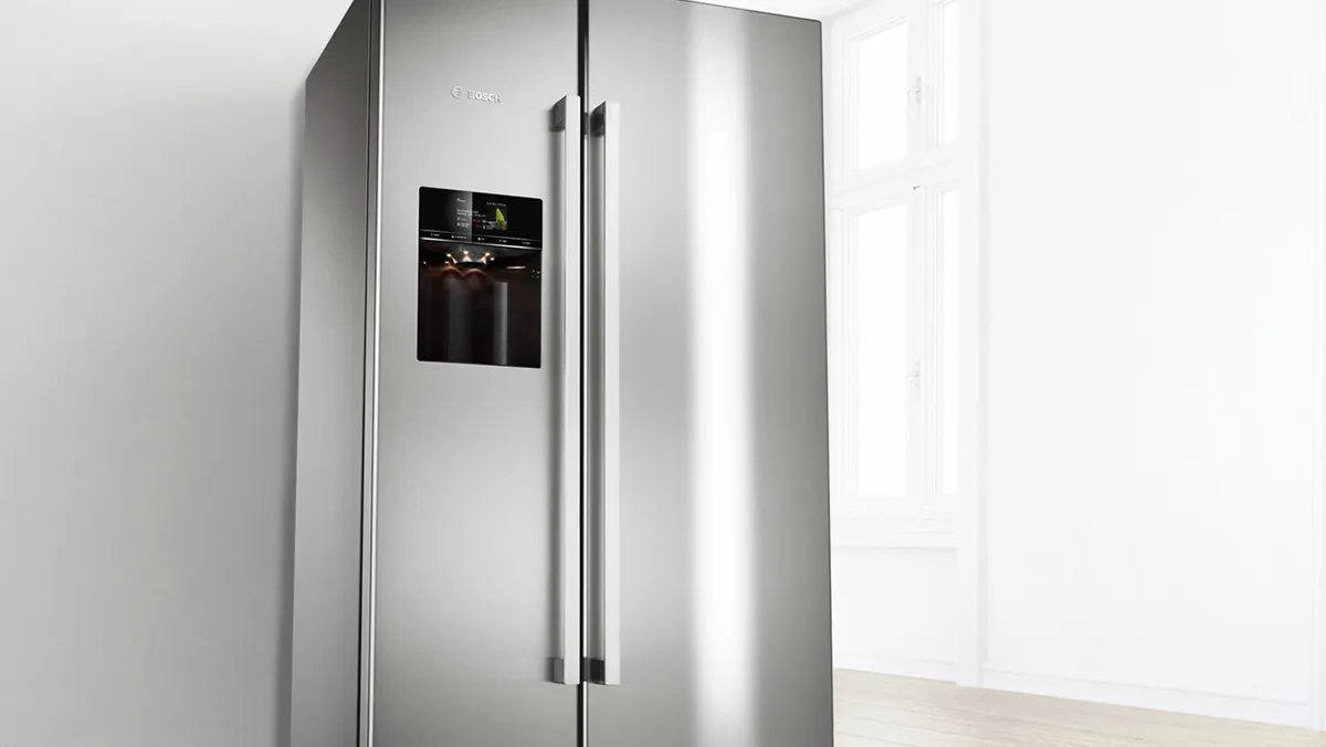 Modern black Bosch refrigerator with double doors, next to a light wood kitchen cabinet.