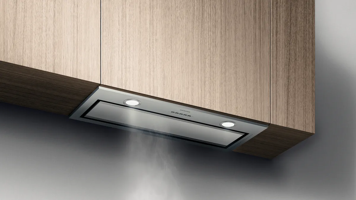 Una cappa da cucina moderna ed elegante integrata negli armadi in legno, con luci LED sottili, che estrae il vapore della cottura sottostante.
