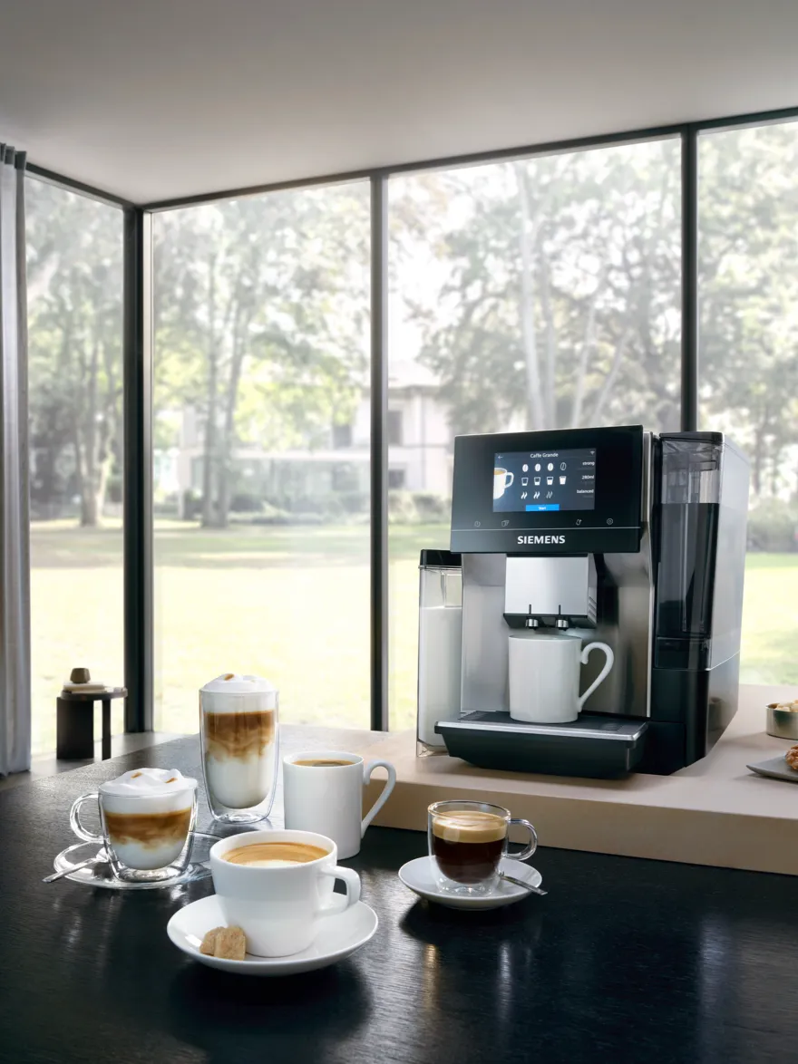 Siemens kavni aparat na mizi z več skodelicami kave okoli njega.