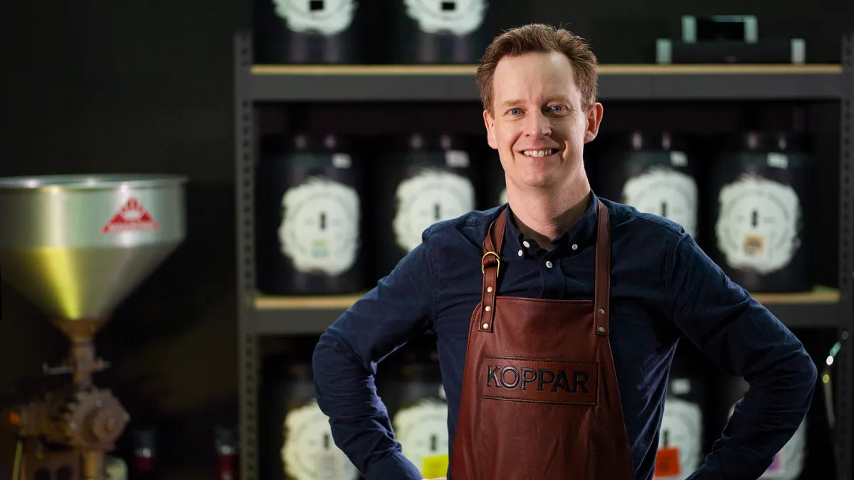 Mand med forklæde står stolt i en kaffebar.