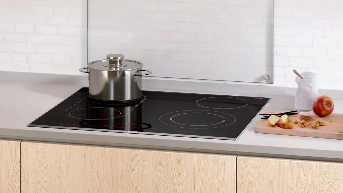 A modern kitchen with a black induction cooktop, a silver pot on the stove, and a cutting board with an apple and chopped nuts.