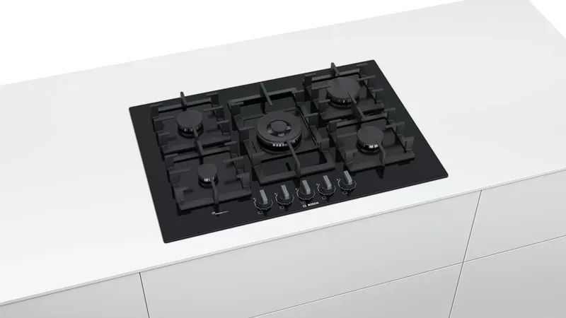 Black gas hob with five burners, including a central wok burner, set into a sleek white kitchen counter. Modern and minimalist design.