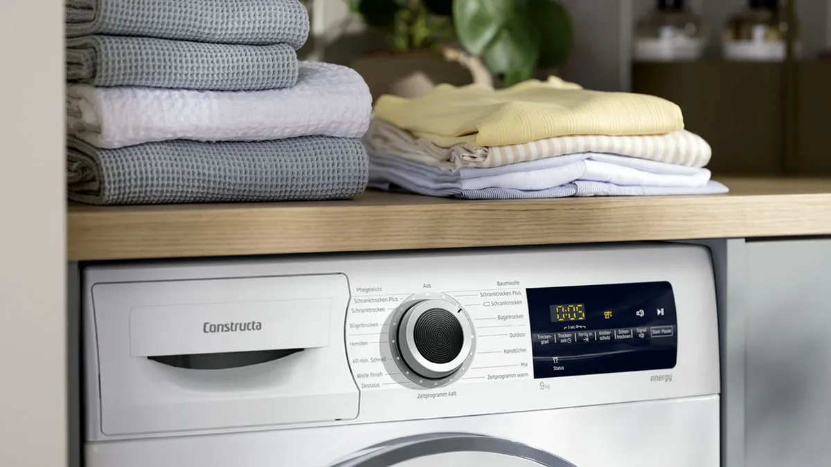 Nahaufnahme des Bedienfelds einer Constructa Waschmaschine. Auf der Ablagefläche darüber liegen gefaltete Wäschestücke.