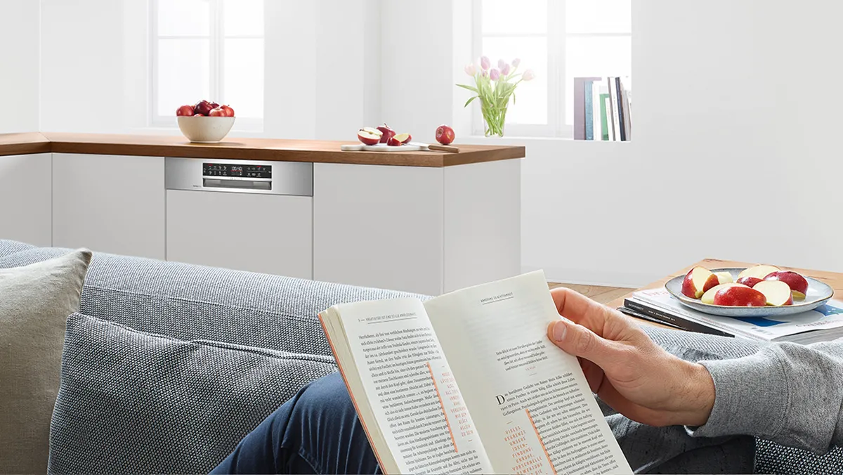 En person, der læser en bog, mens opvaskemaskinen kører.
