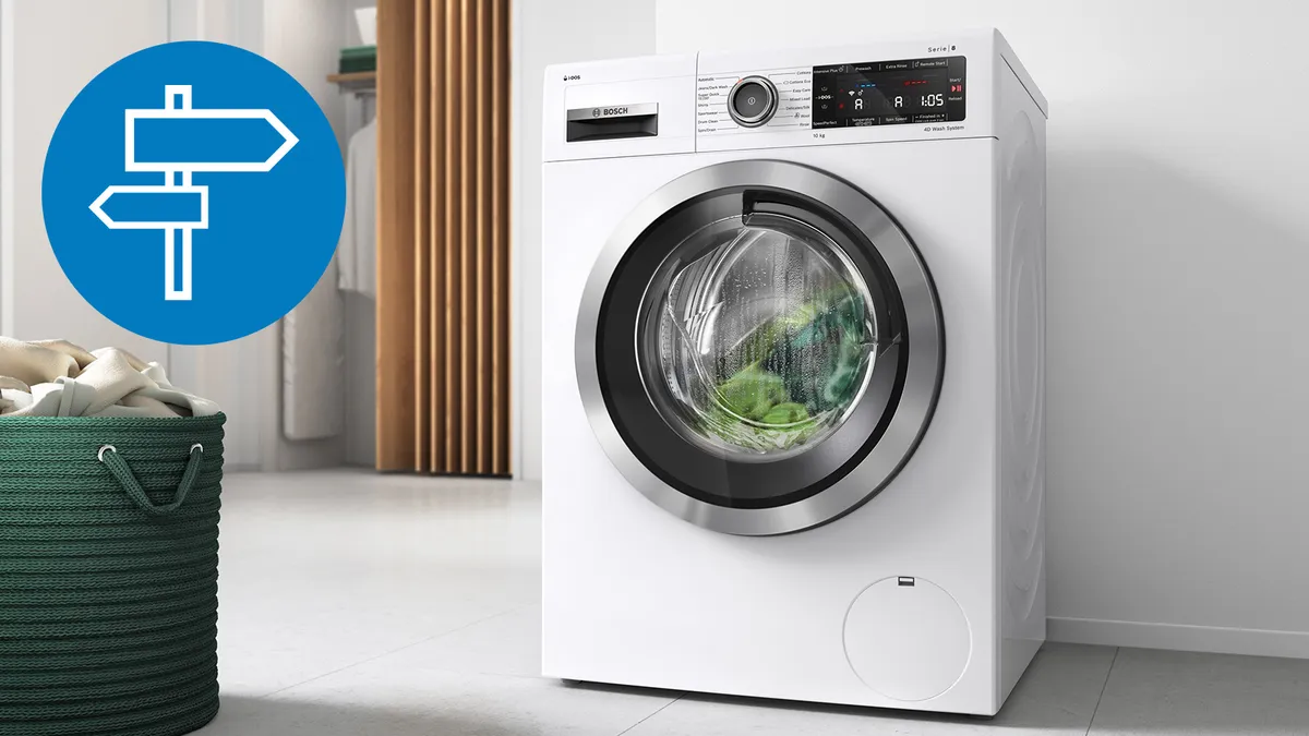 Ένα άσπρο πλυντήριο ρούχων και μπροστά του ένας πράσινος πλεκτός κάδος με άπλυτα.