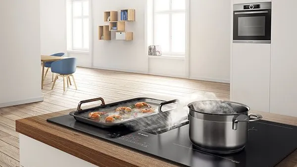 A modern kitchen, featuring boiling pasta and sizzling shrimp on an induction cooktop.
