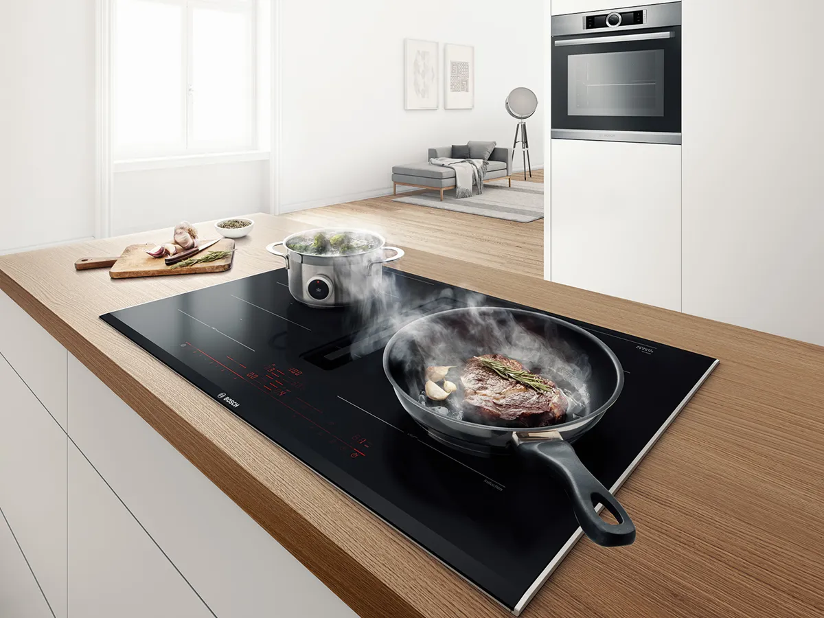 İndüksiyon aşçısı ile modern mutfak, buhar, ahşap tezgah ve cihazlarla yemek.